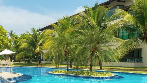 A swimming pool with palm trees and lounge chairs. - Flat 208-C  Condomínio Carneiros Resort (Tamandaré)