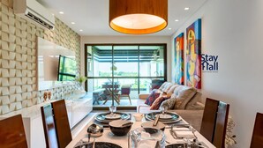 A modern interior with a dining area, a sofa, and a TV on the wall. - Flat 208-C  Condomínio Carneiros Resort (Tamandaré)