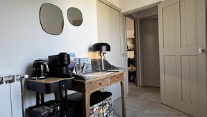A compact workspace with a wooden desk, a coffee maker, a lamp, and a trash bin. - Le 52 en Provence (Robion)