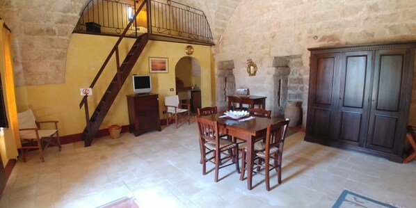 A dining area with a wooden table and chairs, a staircase, and a stone wall. - Masseria la Maestà Ospitalità rurale (Sannicola)