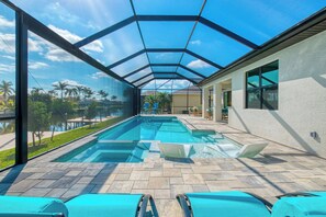 A swimming pool with a glass ceiling, lounge chairs, and a view of palm trees and a lake.