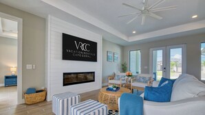 A modern living room with a fireplace, comfortable seating, and a large TV displaying 'VACATION RENTALS CAPE CORALLS'. - VRCC Villa Tiki Oasis (Cape Coral)