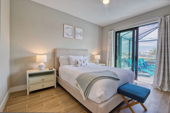 A bedroom with a bed, bedside tables, and a view of a pool area.
