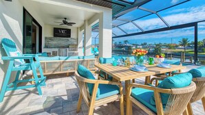A covered outdoor dining area with wicker furniture and a view of the water. - VRCC Villa Tiki Oasis (Cape Coral)