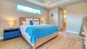 A bedroom with a large bed, two bedside tables with lamps, a ceiling fan, and a window with a view. - VRCC Villa Tiki Oasis (Cape Coral)