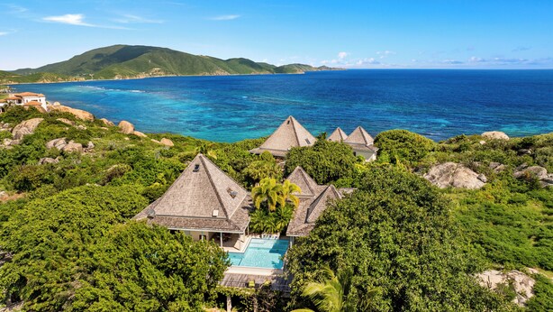 Een resort met meerdere bungalowachtige gebouwen, een zwembad en uitzicht op de oceaan en heuvels.