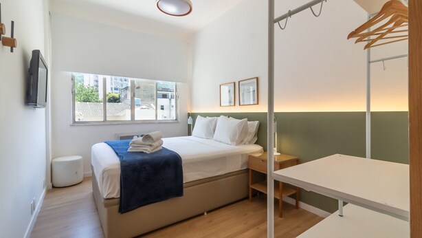 A modern hotel room with a bed, bedside table, and a large window.