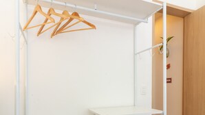 A white metal wardrobe with shelves and a hanging rod, located in a room with wooden flooring and a door in the background.