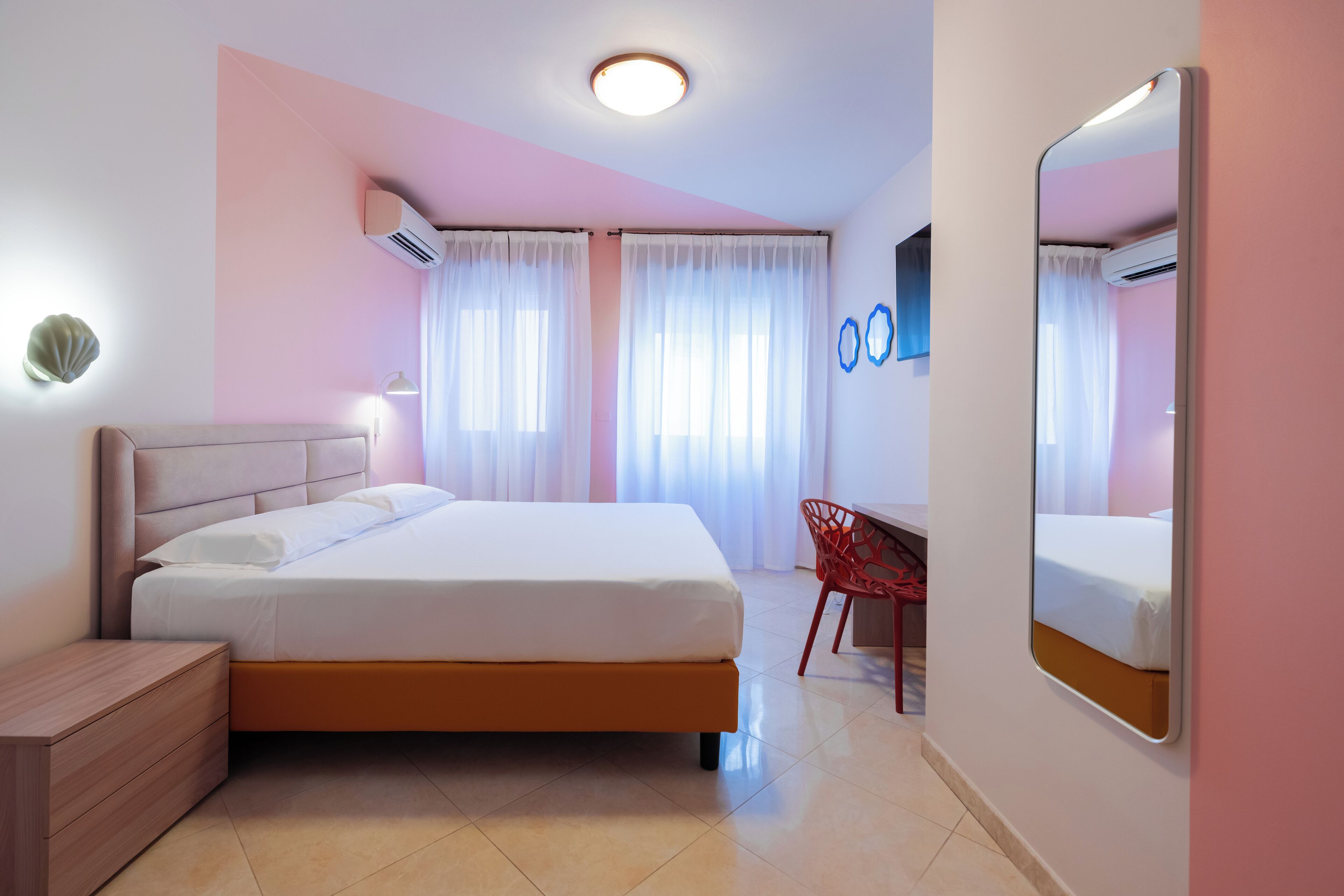 A bedroom with a bed, bedside table, chair, and a large mirror.