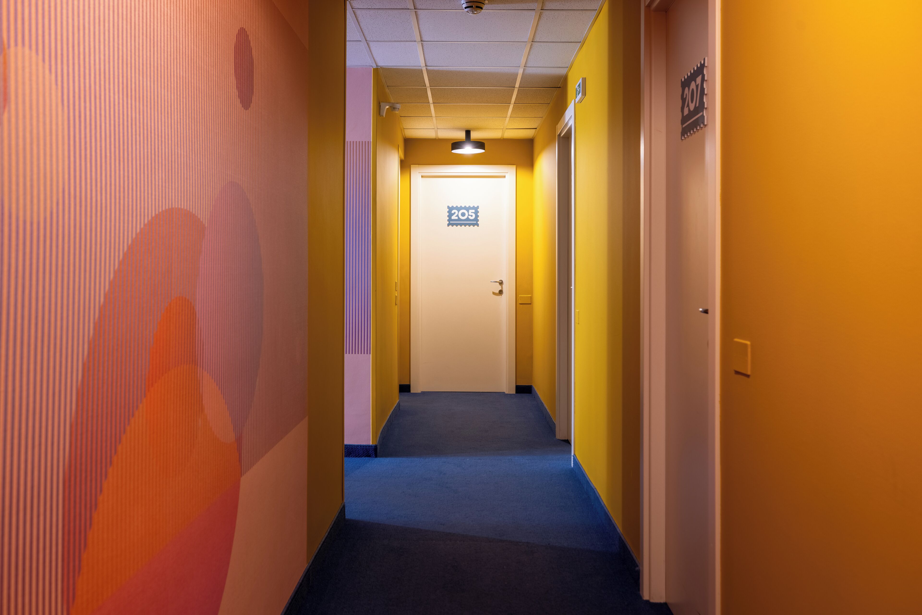 A hallway with a blue carpet, yellow walls, and a door marked with the number 205.