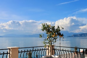 A balcony with a railing, a potted lemon tree, and a view of a lake with mountains in the background. - La Vista Postcard Hotel (Lazise)