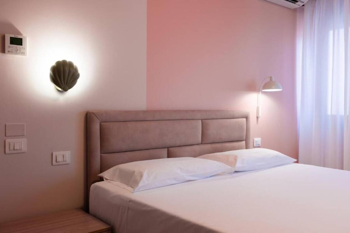 A bedroom with a bed, a nightstand, a wall-mounted light, and a thermostat.