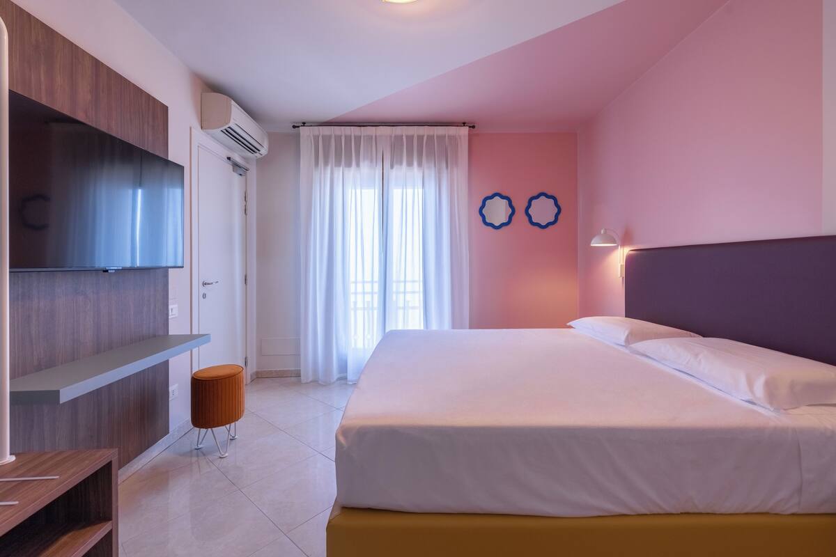 A hotel room with a bed, a TV, a desk, and a window with curtains.
