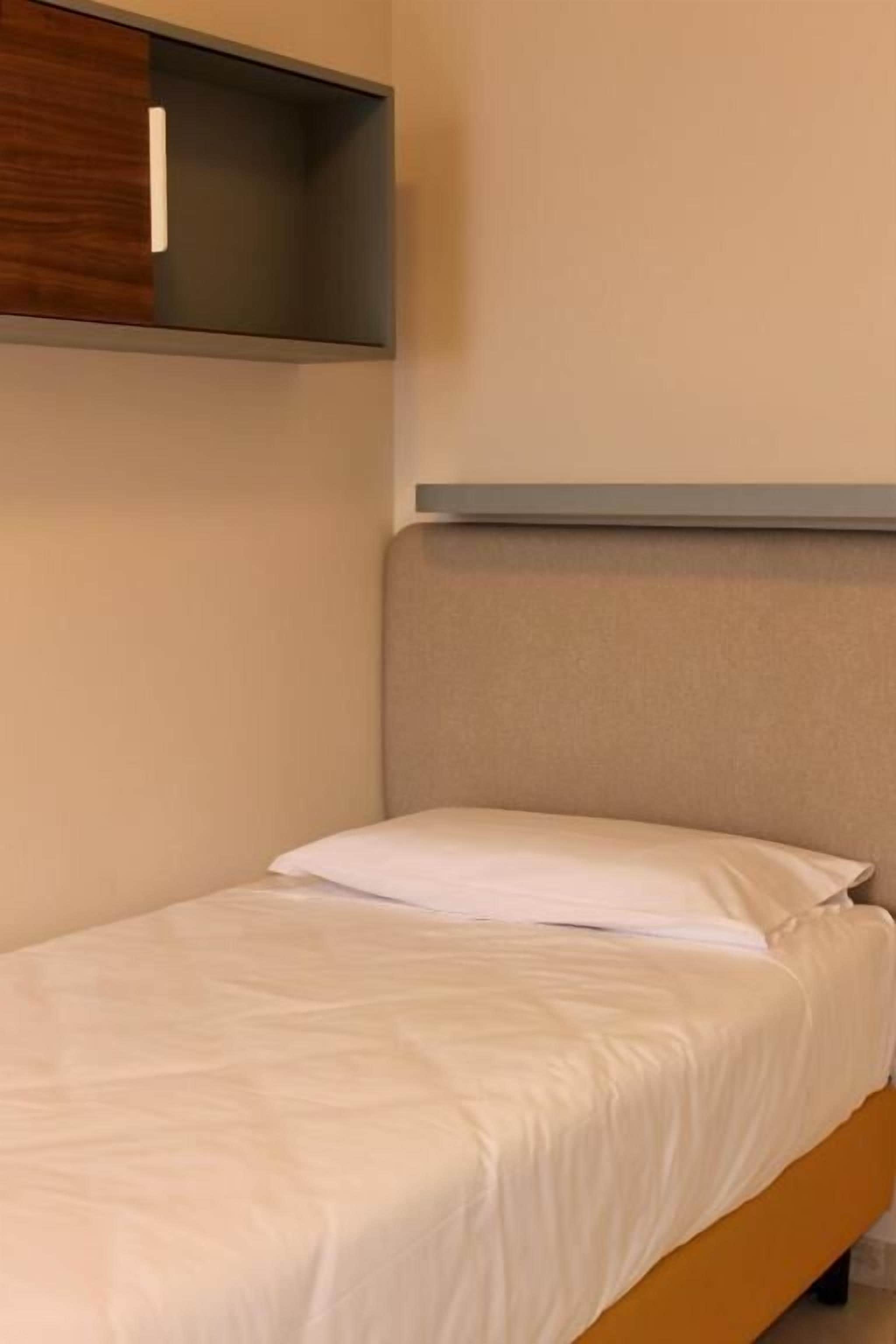 Una cama individual con colchón blanco y cabecera color beige en una habitación con decoración en tonos neutros.