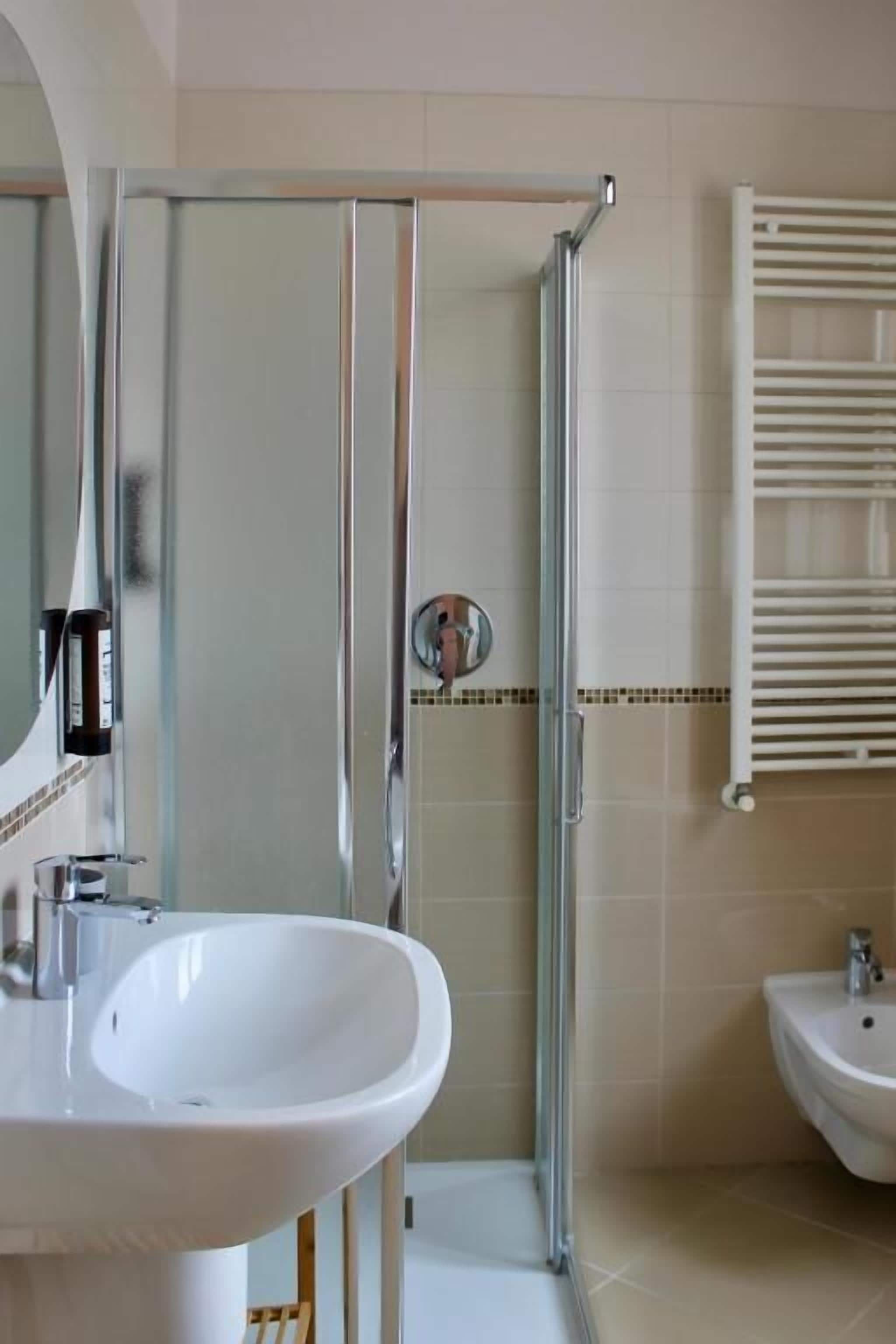 A bathroom with a glass-enclosed shower, a white sink, and a bidet.