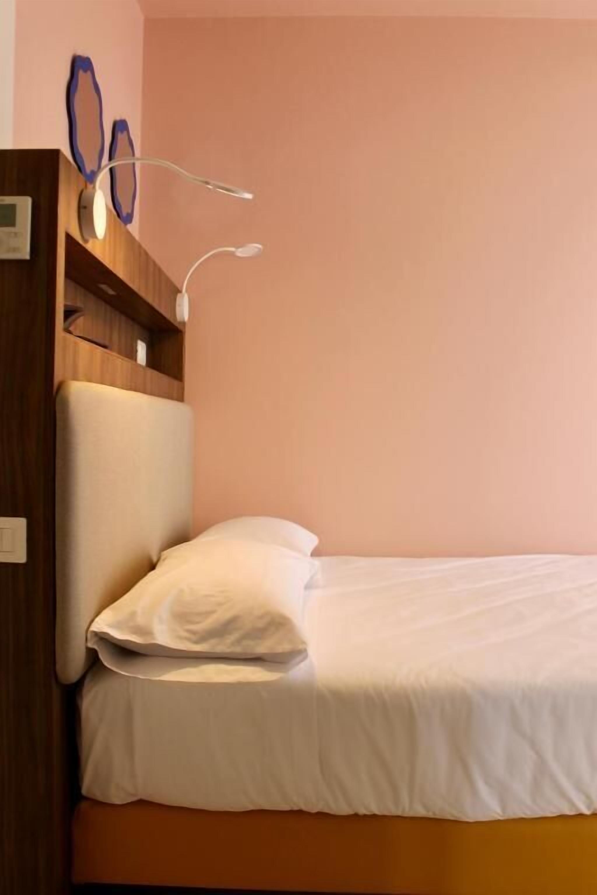 A single bed with white bedding in a room with a wooden headboard and a wall-mounted light fixture.