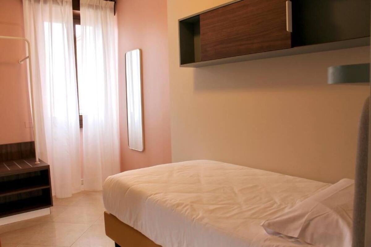 A bedroom with a bed, a wooden nightstand, a mirror, and a built-in shelf above the bed.