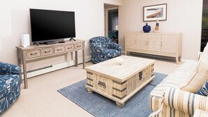 Olohuone, jossa on televisio, puinen kaappi, kuviollinen nojatuoli ja raidallinen sohva.