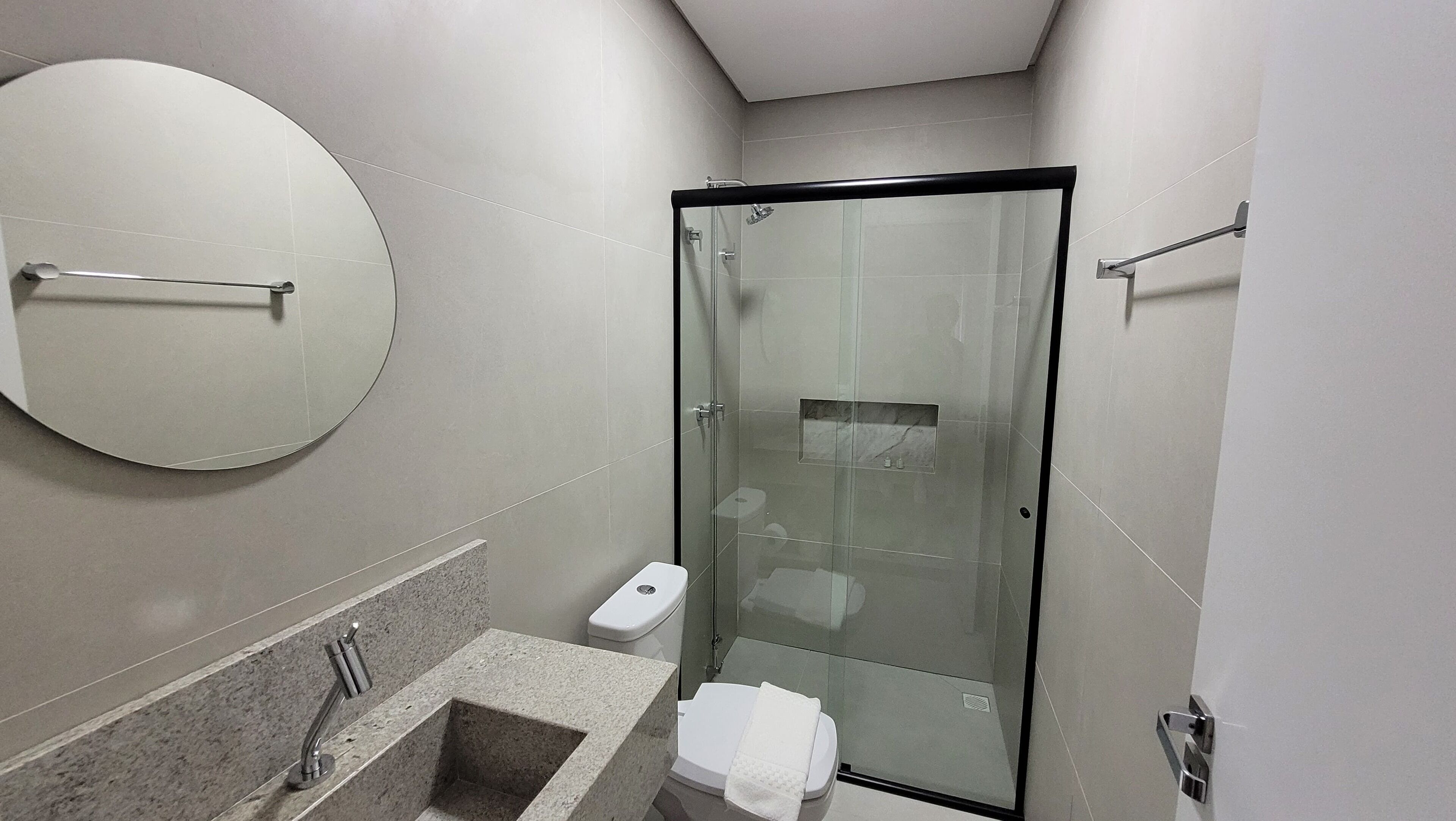 A modern bathroom with a glass-enclosed shower, a round mirror, a marble sink, and a toilet.