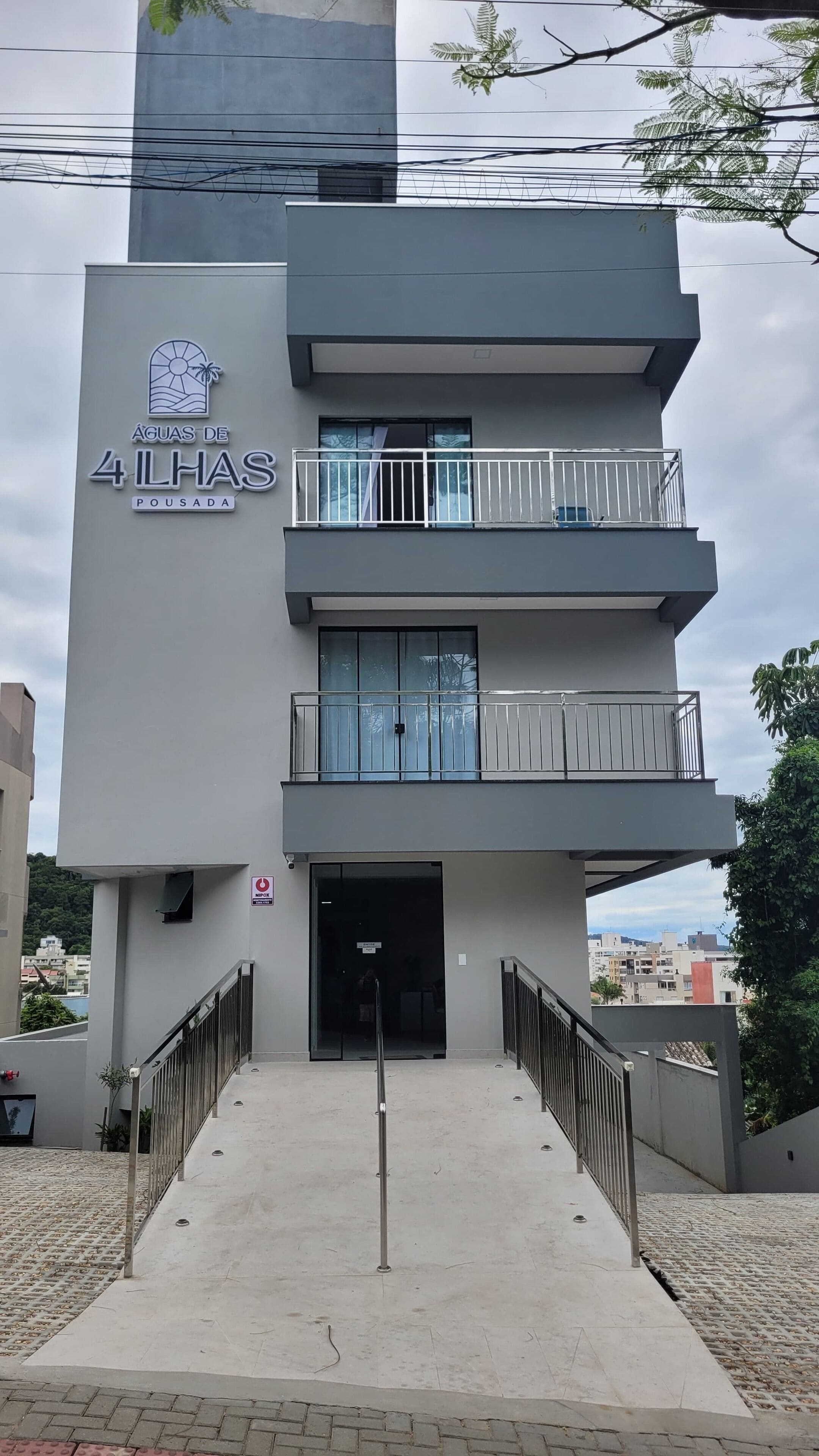 A modern building with a sign reading "ÁGUA DE 4 ILHAS POUSA DA." It features a balcony on the second floor and a gated entrance.