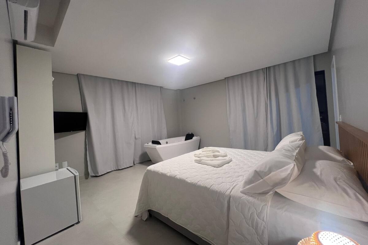 A hotel room with a bed, a bathtub, a desk, and a phone.