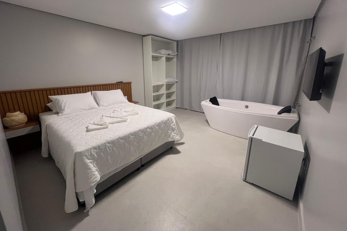 A modern hotel room with a large bed, a built-in bathtub, and a walk-in closet.