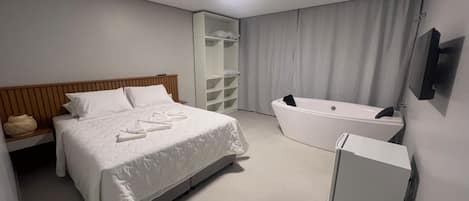 A modern hotel room with a large bed, a built-in bathtub, and a walk-in closet.