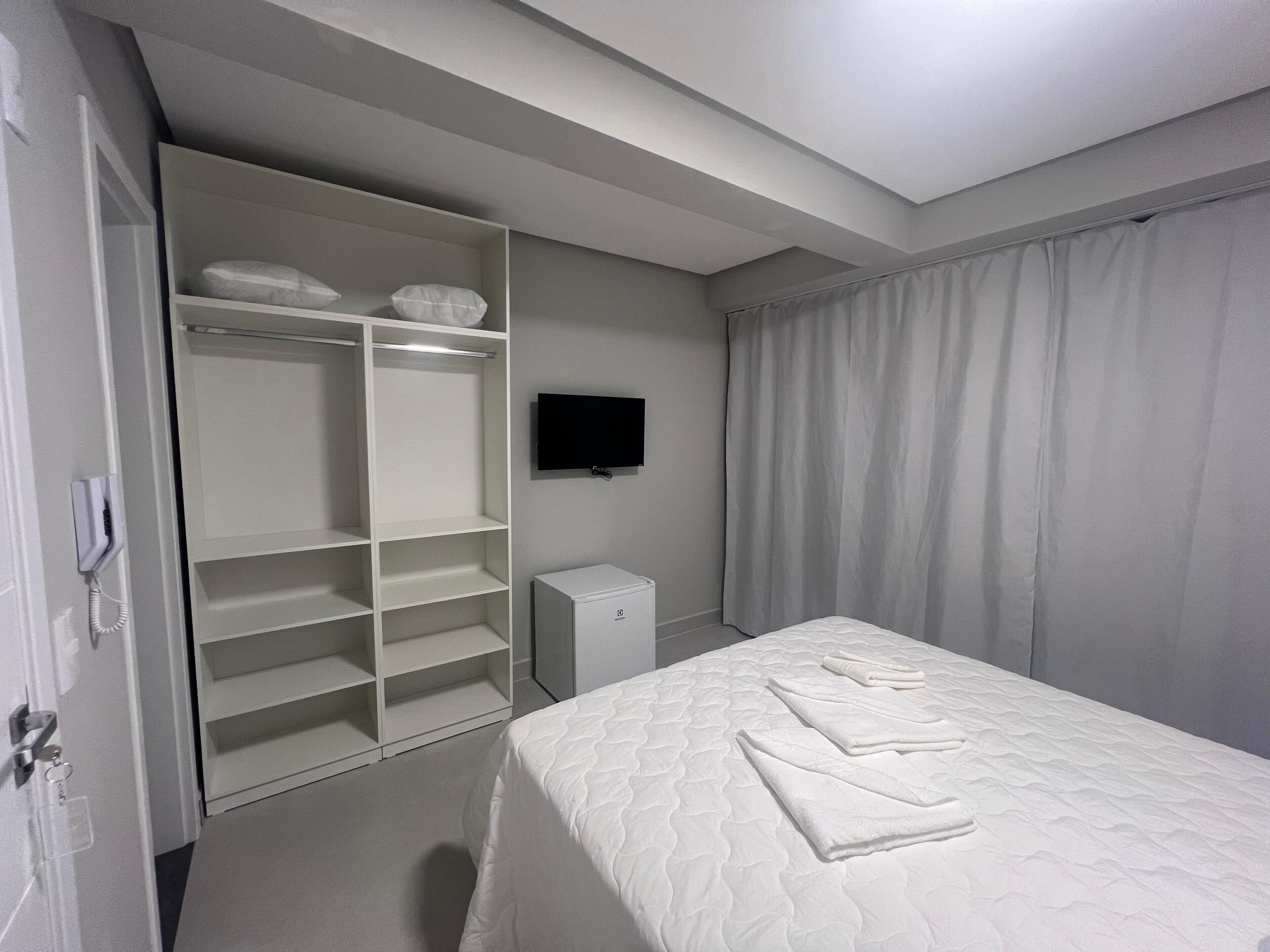 A hotel room with a bed, a wardrobe, a television, and a small cabinet.