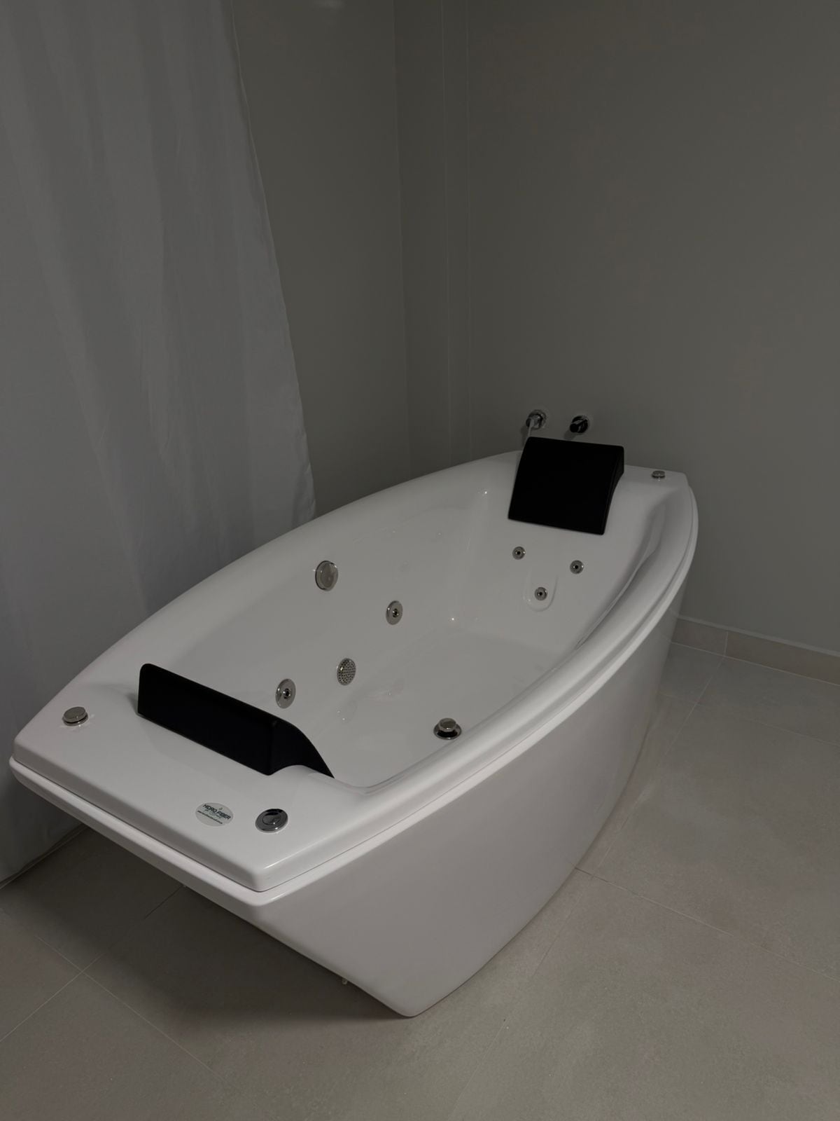 Una bañera moderna, blanca y independiente con múltiples jets, un panel de control y un pequeño estante.