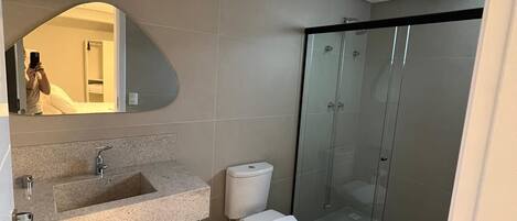 A modern bathroom with a large mirror, a granite sink, a toilet, and a glass-enclosed shower.