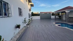 A spacious outdoor area with a swimming pool, a covered patio, and a white building with multiple windows and a garage.