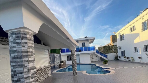 A modern outdoor pool area with a stone pillar, a blue pool, and a clear sky.