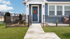Una casa con puerta principal, una corona decorativa, un pequeño jardín y una cerca de metal.