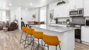 Una cocina moderna con armarios blancos, una isla central con taburetes y horno empotrado además de un microondas.