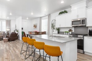 Una cucina moderna con mobili bianchi, un'isola centrale con sgabelli da bar, forno a incasso e forno a microonde.