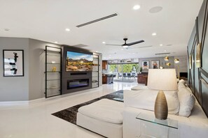 A modern living room with a flat-screen TV, a ceiling fan, and a dining area with a glass table.