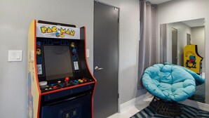 Una habitación con una máquina arcade Pac-Man, un sillón informal azul y una puerta.