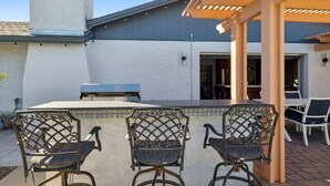 Un patio exterior con una pérgola, una parrilla y tres sillas.