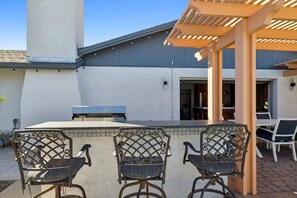 An outdoor patio with a pergola, a grill, and three chairs.