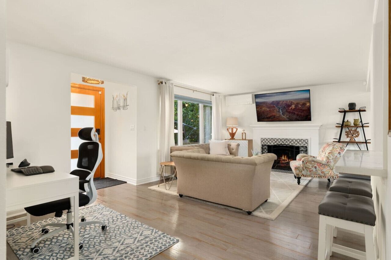 Un salon moderne avec une cheminée, un canapé, un bureau avec une chaise et un téléviseur fixé au mur.