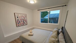 Ein Schlafzimmer mit Bett, Fenster, Deckenleuchte und einem Wandbild.