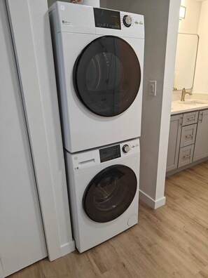 Un appareil combiné lave-linge et sèche-linge, installé en hauteur, dans une cuisine avec un plancher en bois et un comptoir blanc doté d’un évier.
