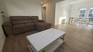 Ein modernes Wohnzimmer mit einem weißen Couchtisch, einem braunen Sofa und einem Essbereich mit weißen Stühlen.