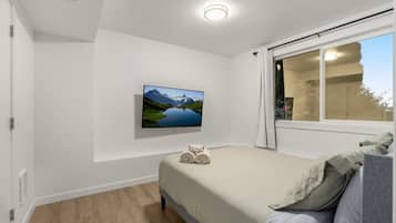 Un dormitorio con una cama, televisión montada en la pared y una ventana con cortinas.