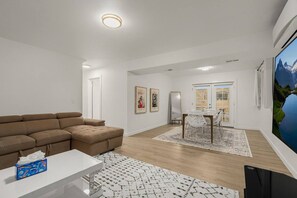 Ein modernes Wohnzimmer mit einem Ecksofa, einem Esstisch mit Stühlen und einem an der Wand befestigten Flachbildfernseher.