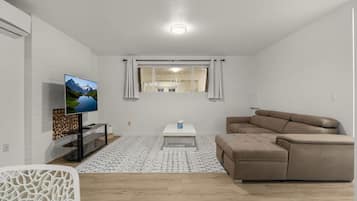 Una sala de estar moderna con un televisor de pantalla plana, un sofá color beige, una mesa de centro y una alfombra estampada.