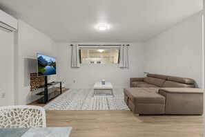 A modern living room with a flat-screen TV, a beige sofa, a coffee table, and a patterned rug. - 2BR Lux Apartment | 5 Mins from Airport | Pets+ (Burien)
