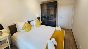 Una habitación de hotel con cama, mesita de noche, armario y un banco de madera con toallas.