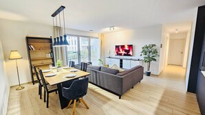 Una sala de estar moderna con un sofá, una mesa de comedor con sillas, un televisor montado en la pared y una estantería.
