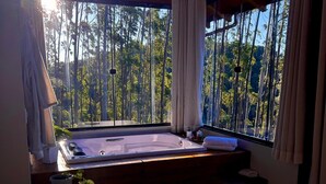 Une pièce dotée d’une grande fenêtre, d’un banc en bois, d’une petite table avec une plante et d’un bain à remous.